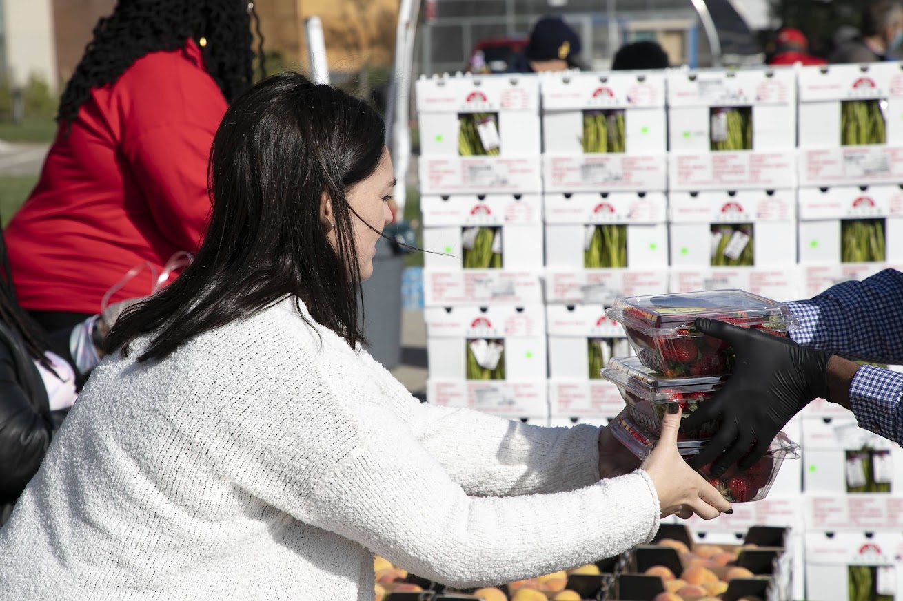 Woman handing containers of fresh strawberries to a gloved volunteer at a food distribution