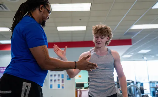 YMCA coach in blue shirt greeting a smiling young man during a fitness coaching session