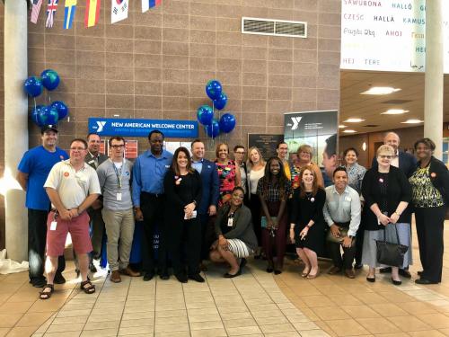 Event attendees and Y staff gather for a photo in front of the New American Welcome Center.