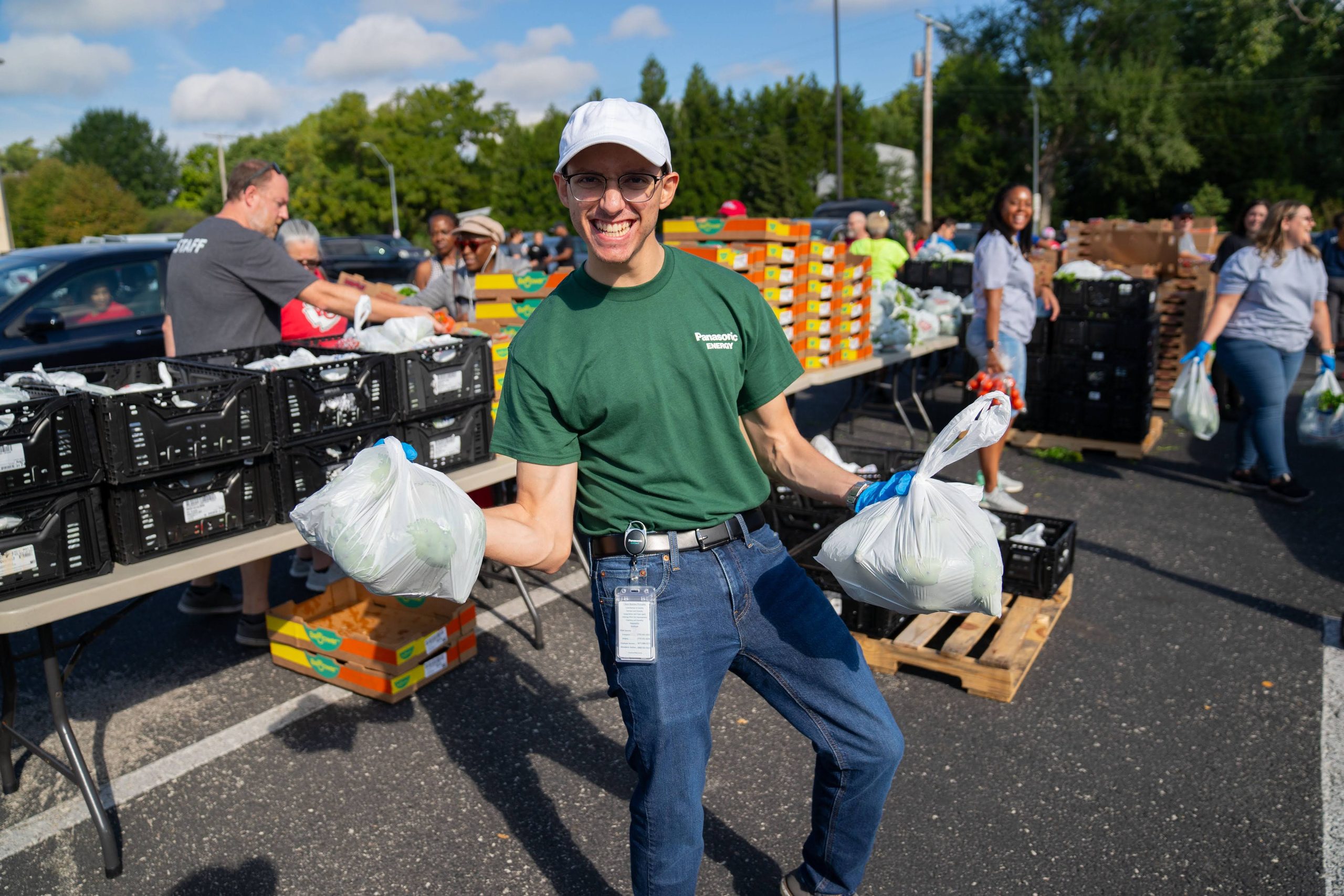 Smiling volunteer carrying bags of fresh produce at an outdoor food distribution