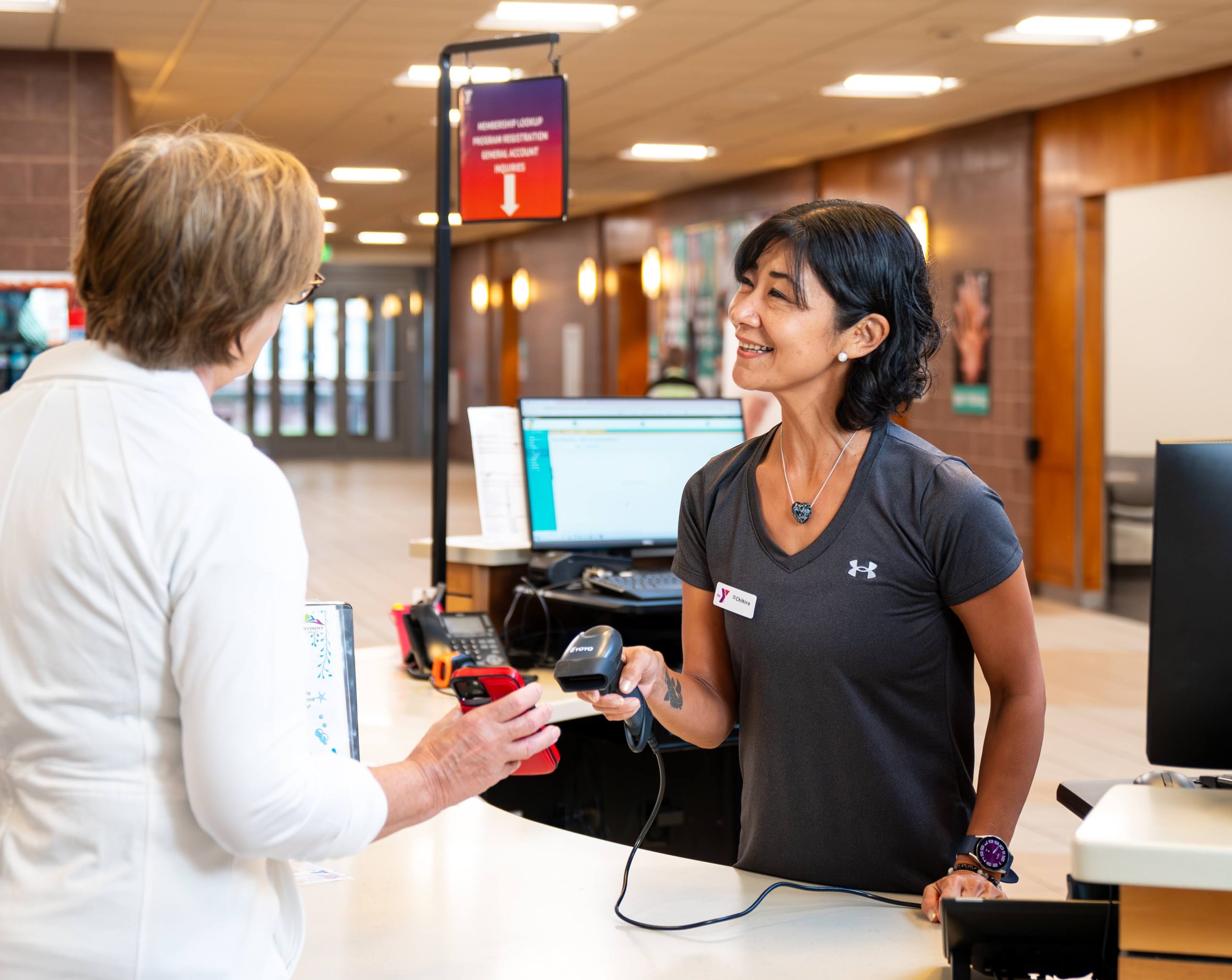 Smiling YMCA staff member helps a member check in at the front desk