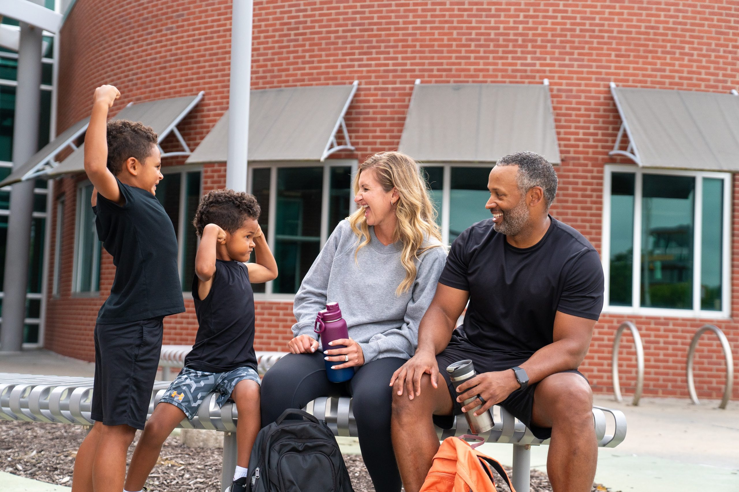Parents and two young boys laughing together on a bench outside a YMCA branch