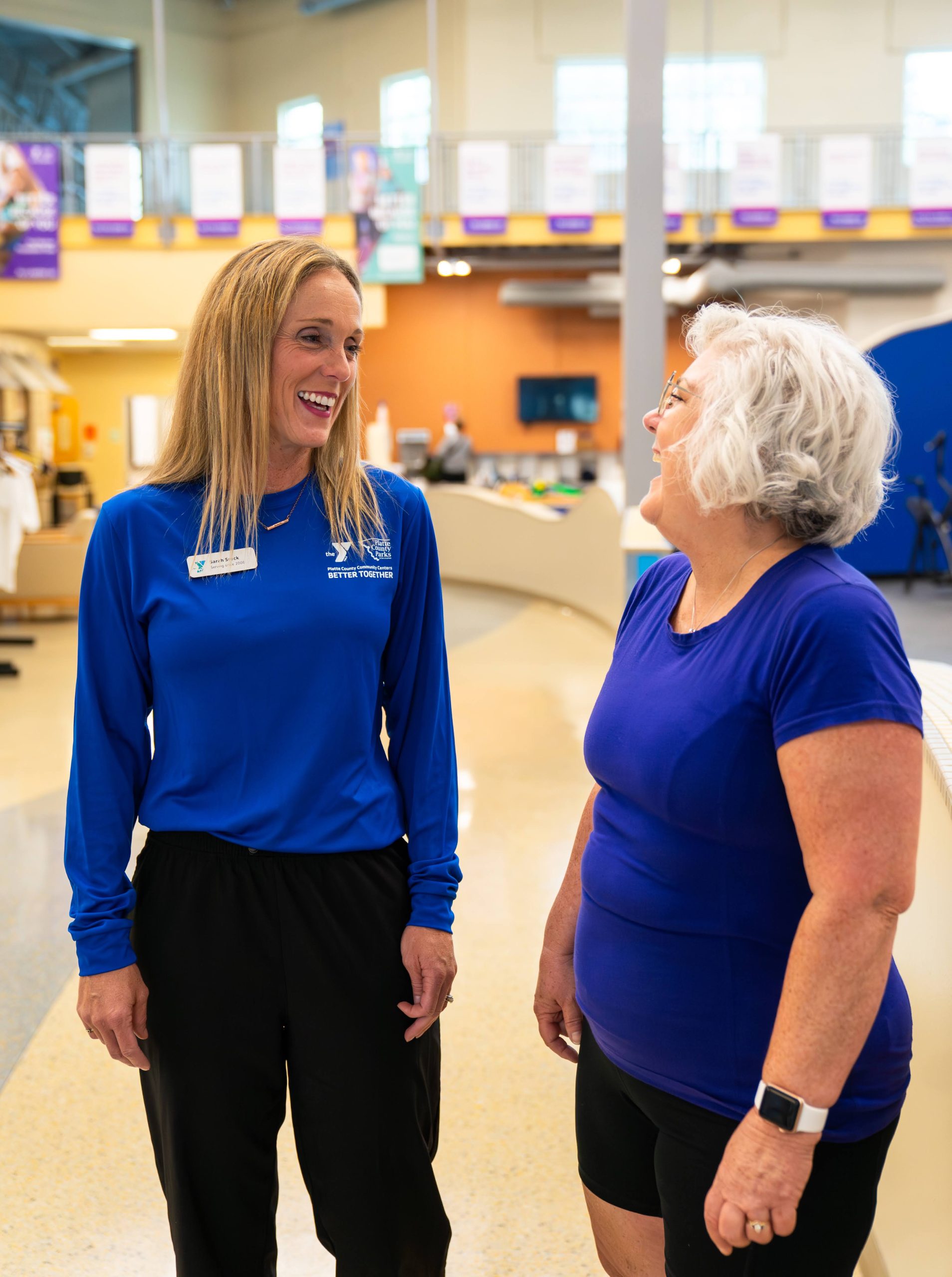 YMCA wellness coach in blue shirt talking and laughing with an older woman member