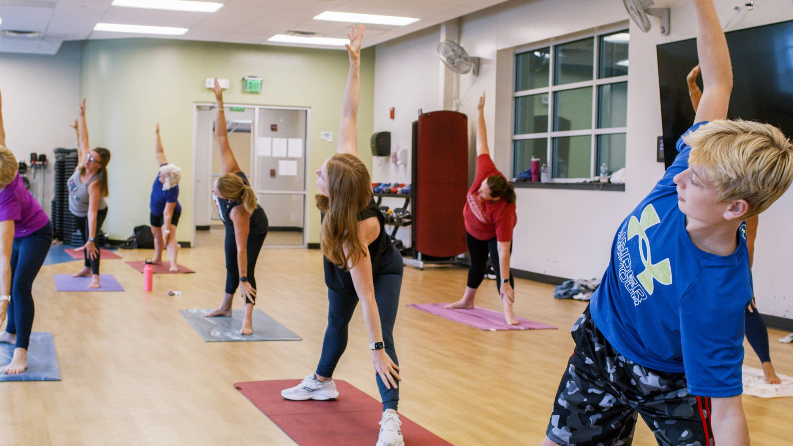 Group fitness class members stretching sideways with arms overhead on mats in a studio