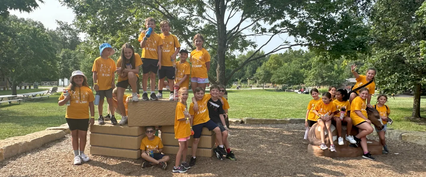 Campers in yellow shirts climbing and posing on wooden play structure in a park