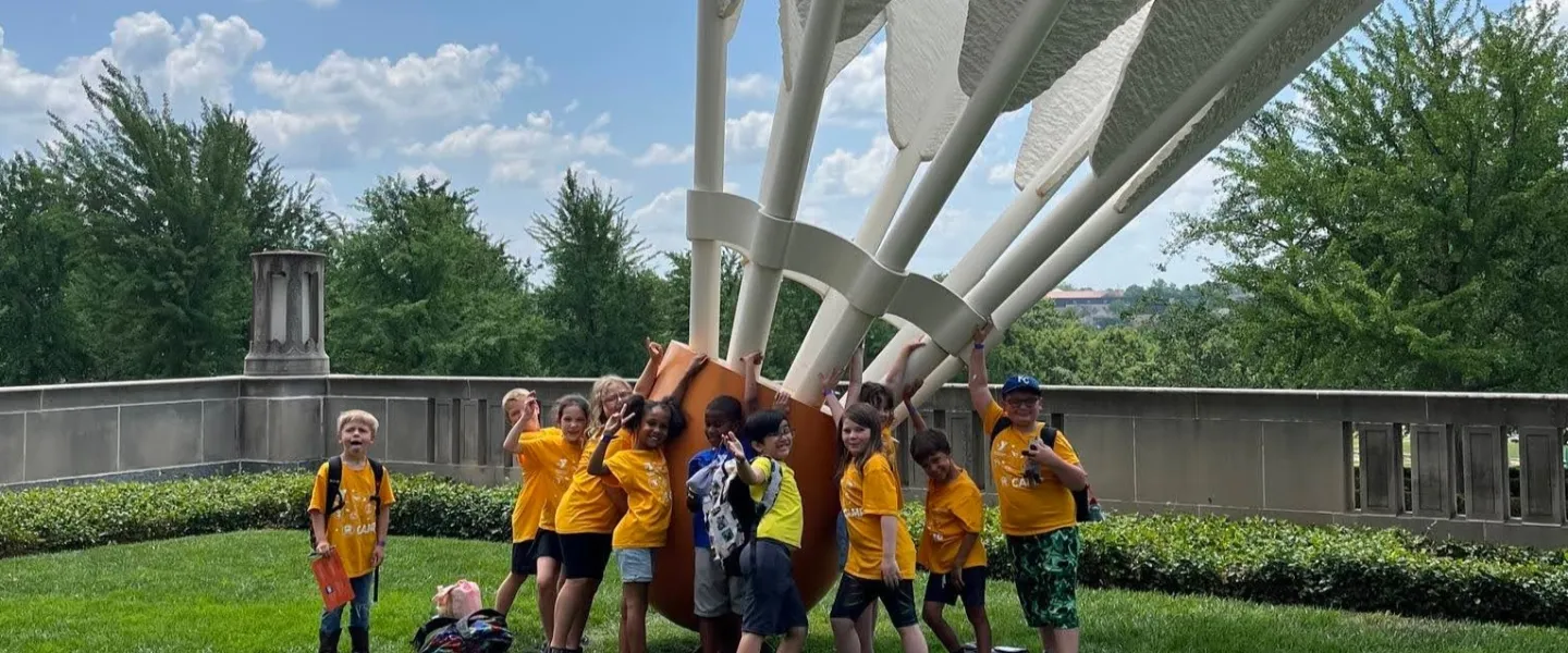 Group of campers in yellow shirts posing outdoors under a white sculptural canopy