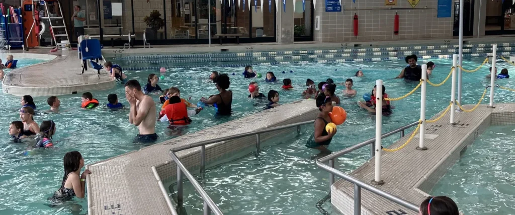 Many children in an indoor pool with counselors during a summer camp swim session