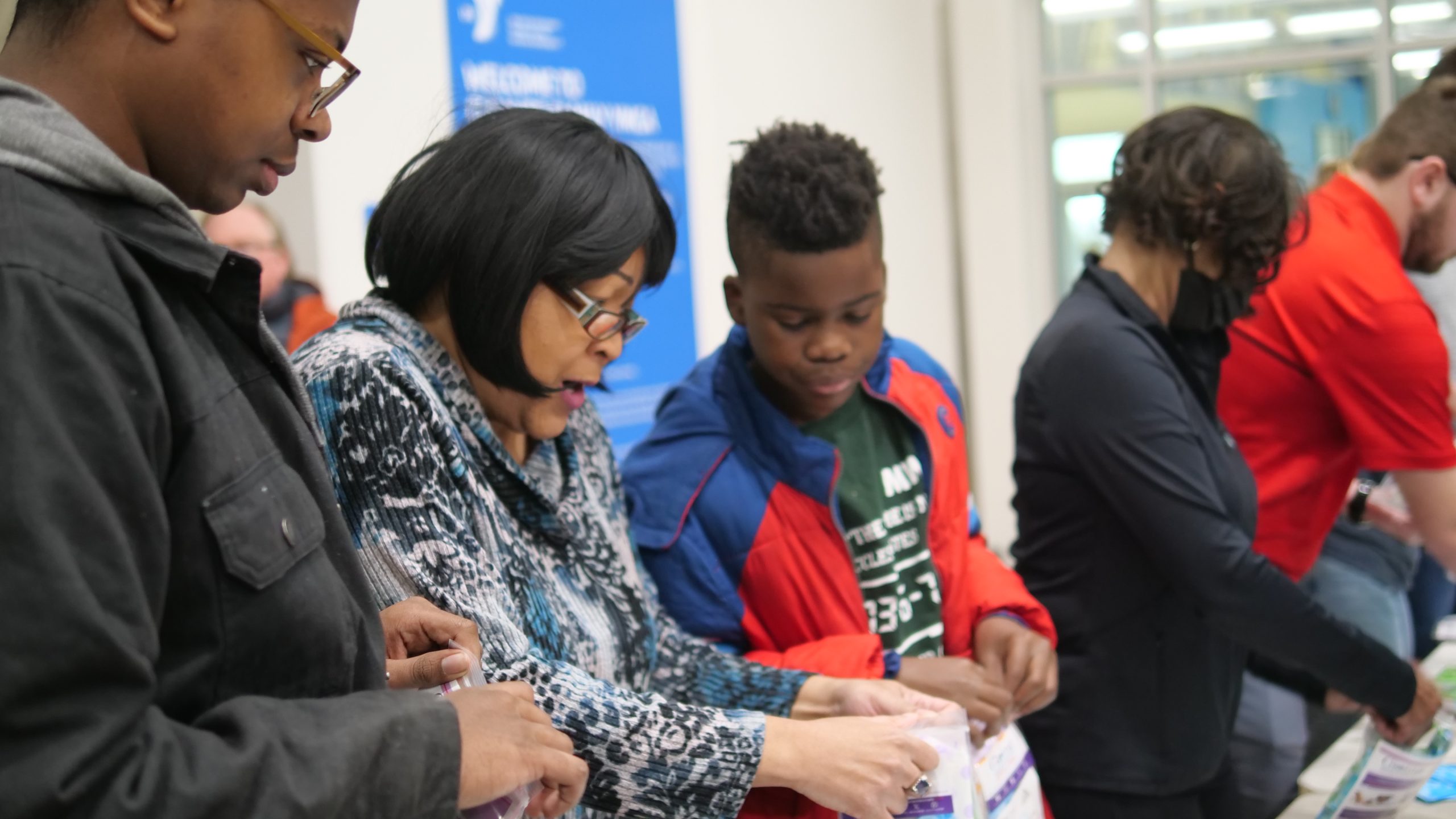 A family fills bags together at a welcome table inside a YMCA lobby