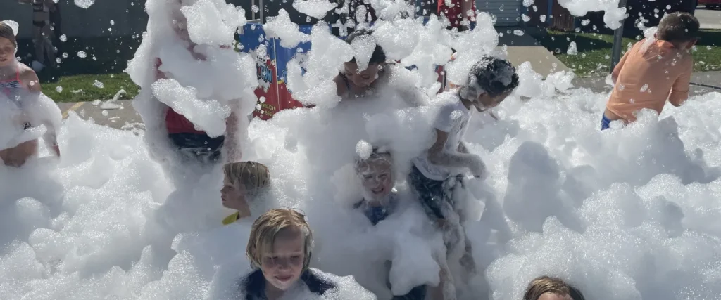 Children laughing and playing in a giant outdoor foam pit at summer camp