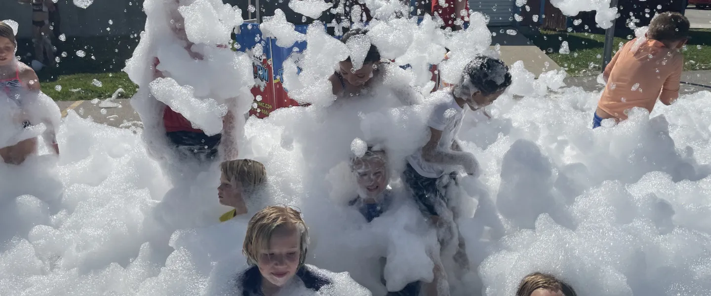 Children laughing and playing in a giant outdoor foam pit at summer camp