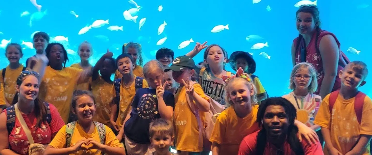 Summer camp kids and counselors posing in front of a large aquarium tank with fish