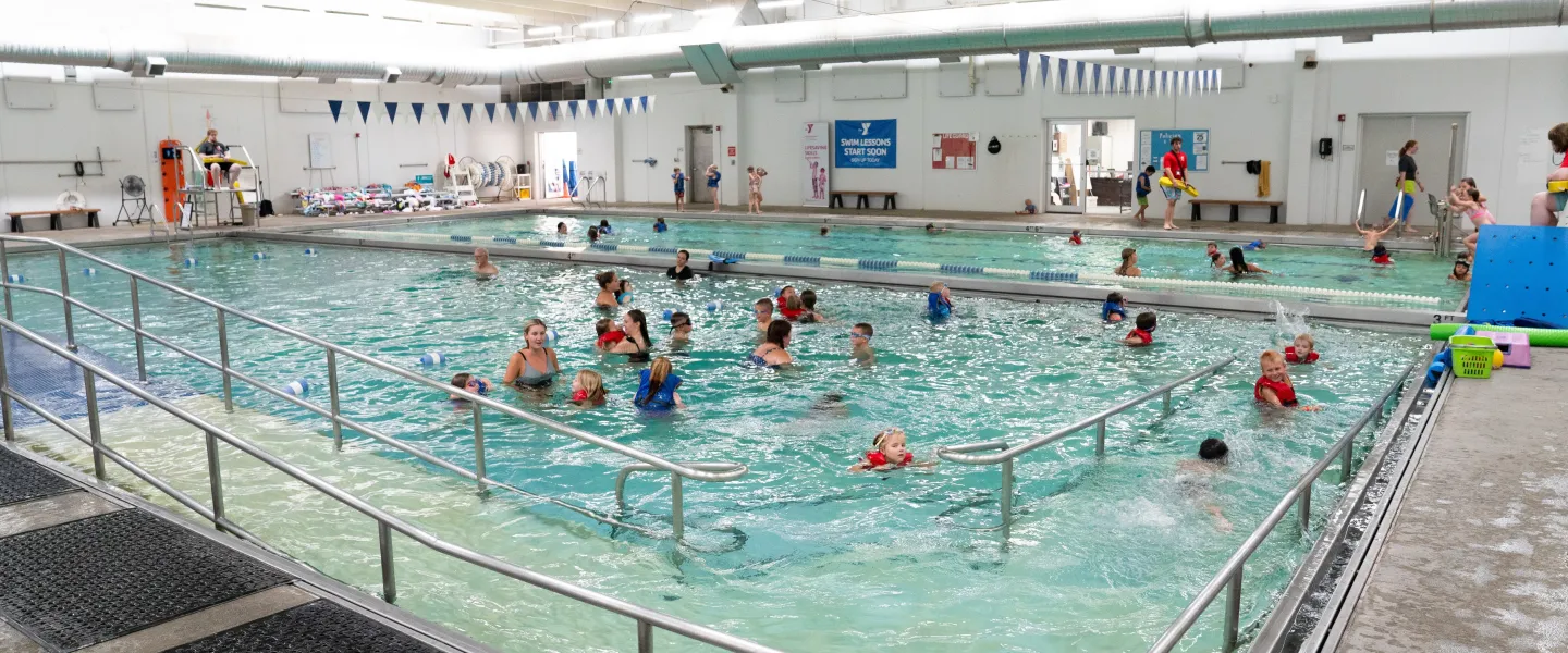 Children and families swimming in a large indoor YMCA pool with metal railings