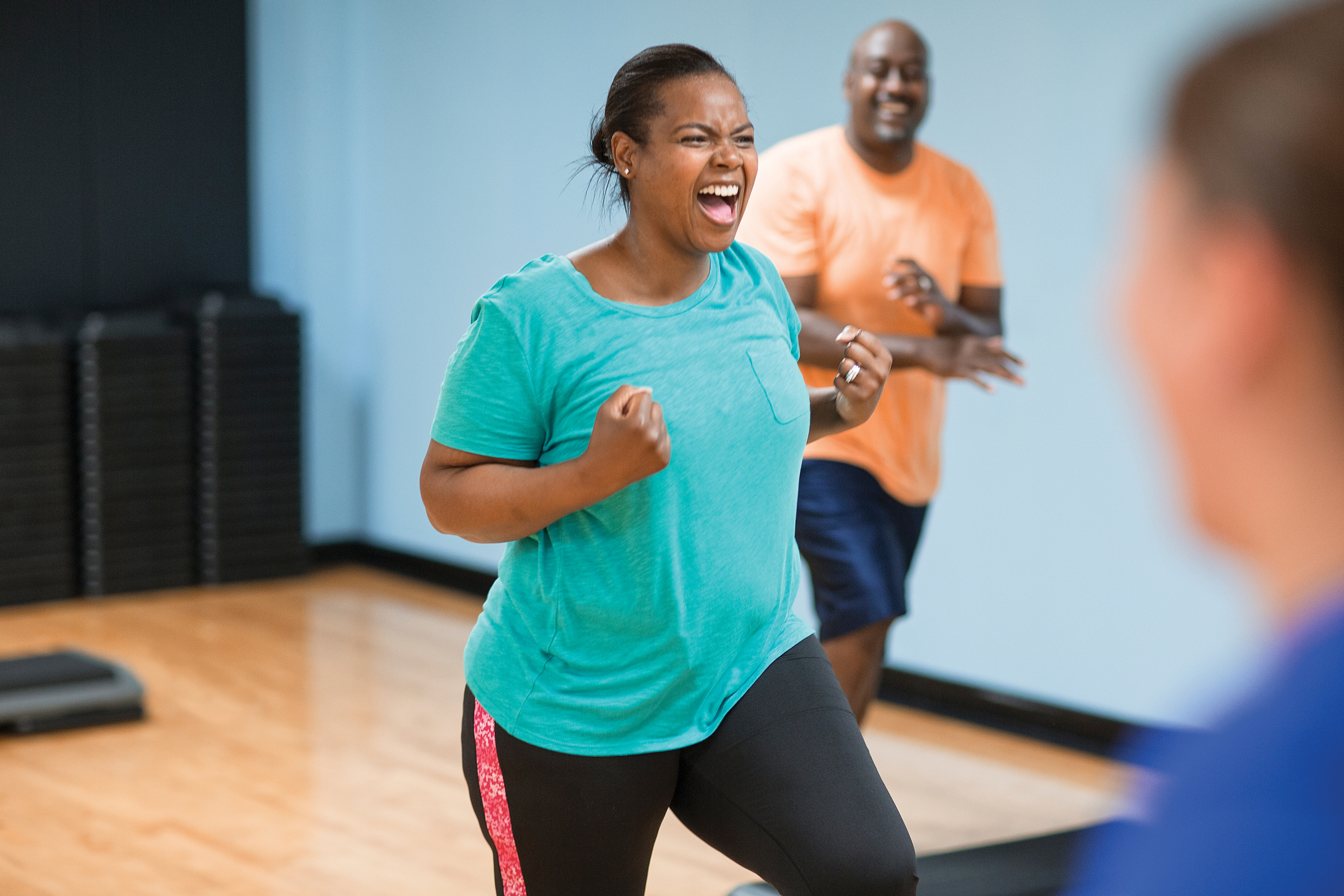 Woman cheering with clenched fists in a group fitness class, man behind her