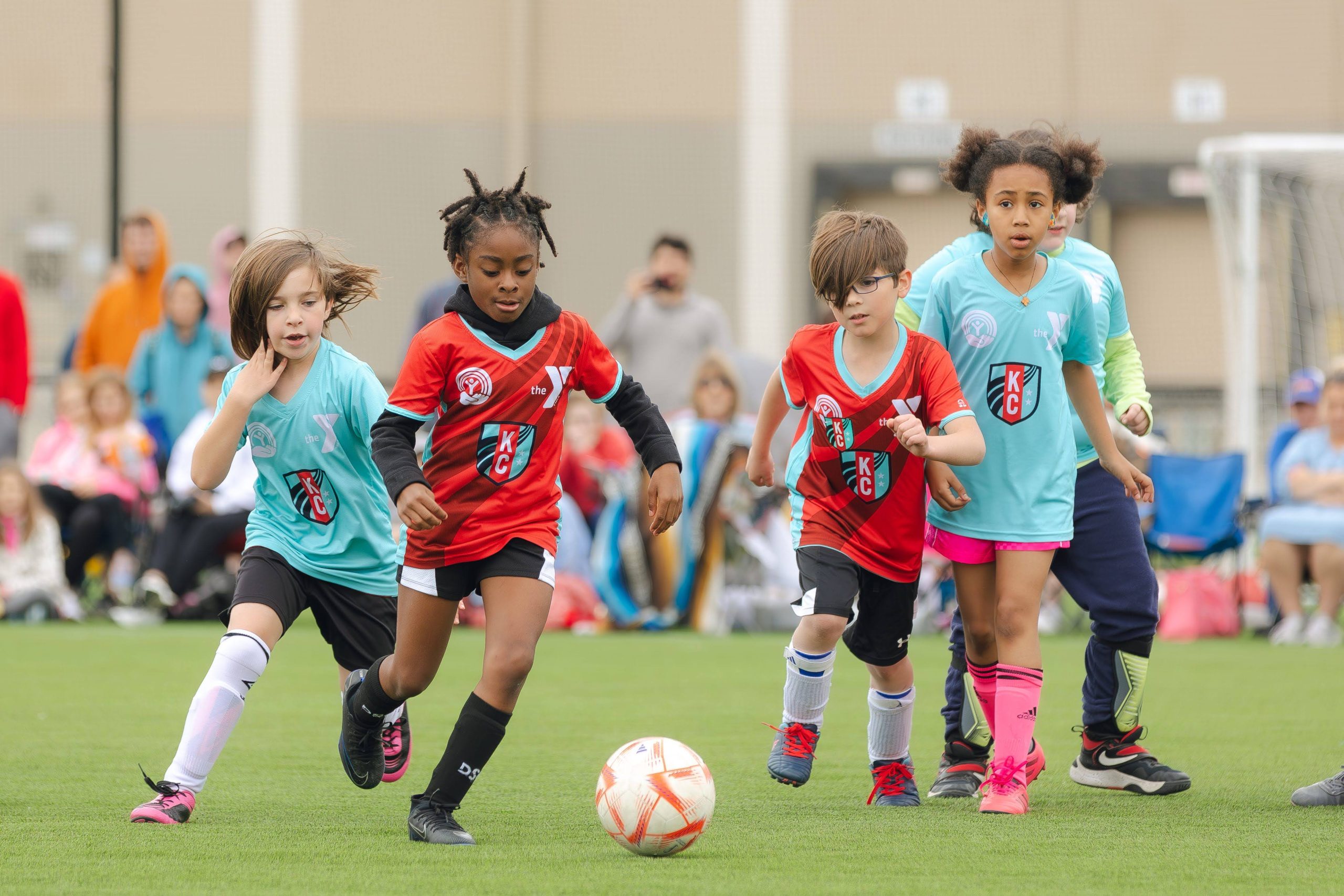 Young children in KC soccer jerseys chase a ball during a youth match