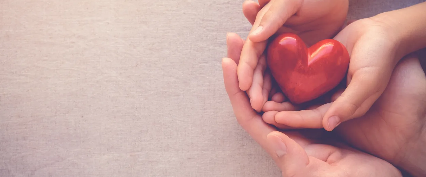 Adult and child hands cradling a small red heart against a soft neutral background