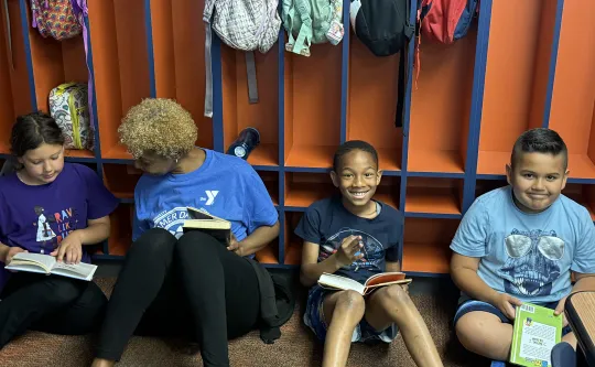 Four children and a mentor reading books while sitting against colorful cubby lockers