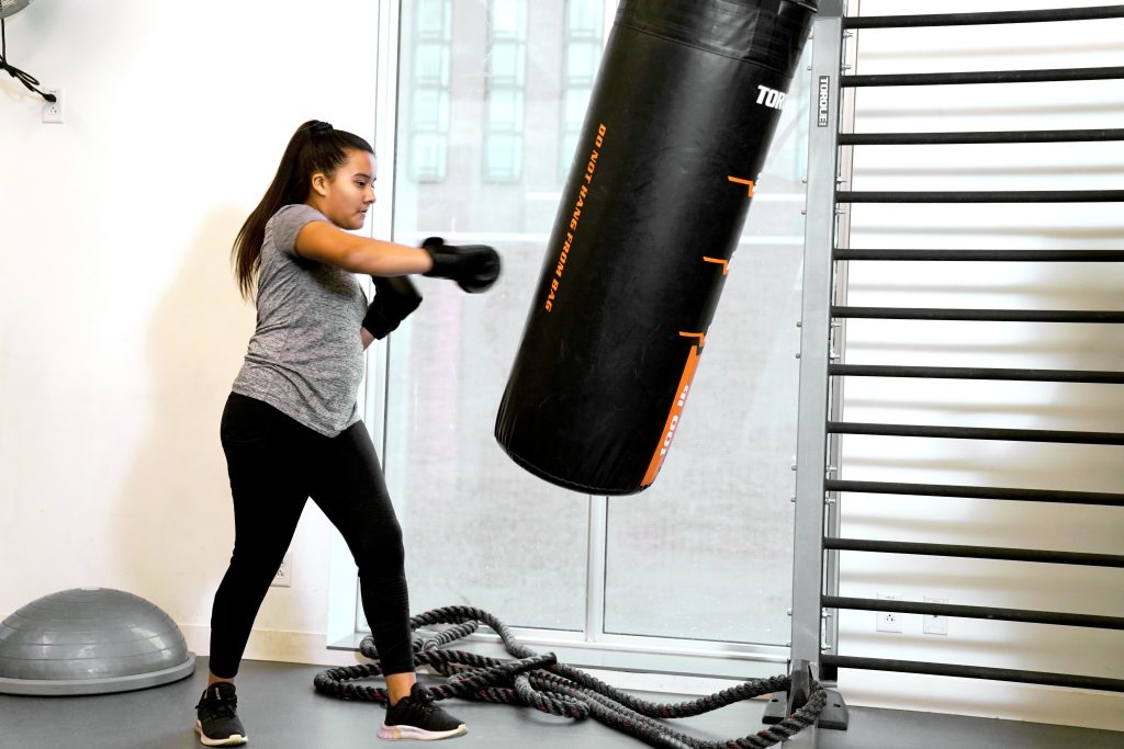 Woman in athletic wear boxing a heavy bag with gloves in a bright fitness studio