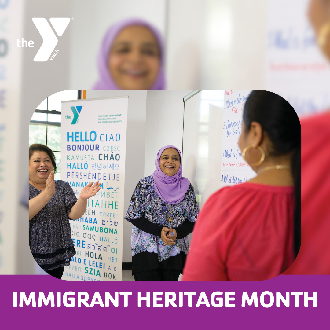 Kansas City YMCA graphic featuring two women smiling and clapping their hands to a person whose back is facing the camera. They are in front of a YMCA sign saying "hello" in many different languages. There's a bottom text banner saying "Immigrant Heritage Month".