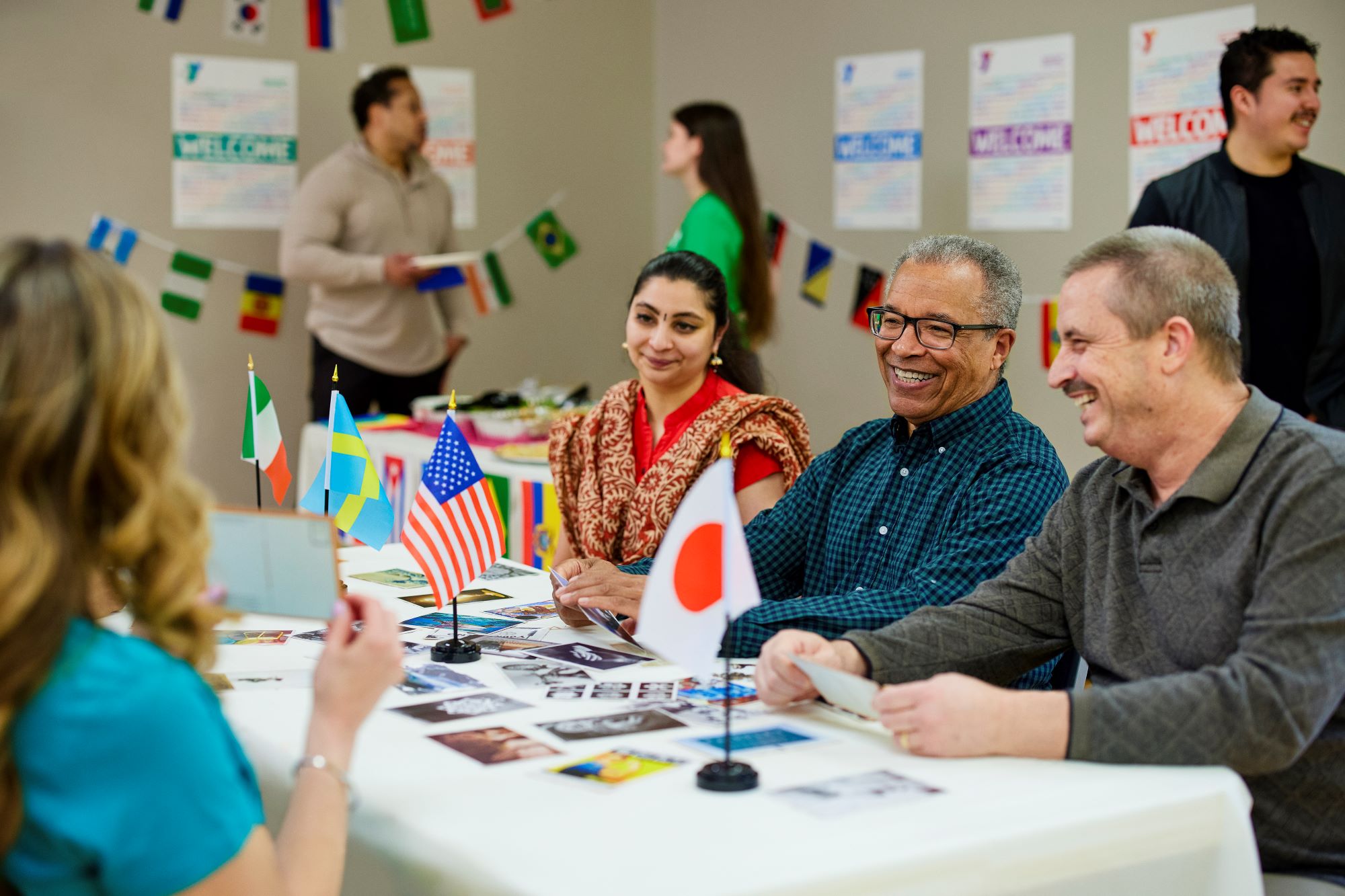 People of multiple nationality sit across from each other at a table covered in multiple countries' flags at a Kansas City YMCA.