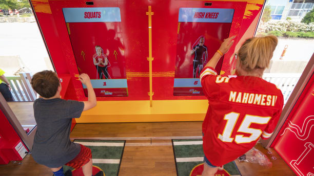 Woman in Mahomes Kansas City Chief's jersey and child working out in front of Chiefs Training Lab Powered by GEHA.