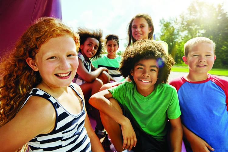Six kids are gathered together outside smiling at the camera