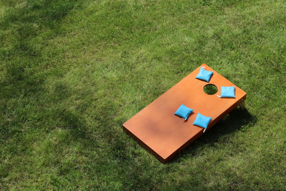 Cornhole board on green grass with 4 blue cornhole bean bags on the board.