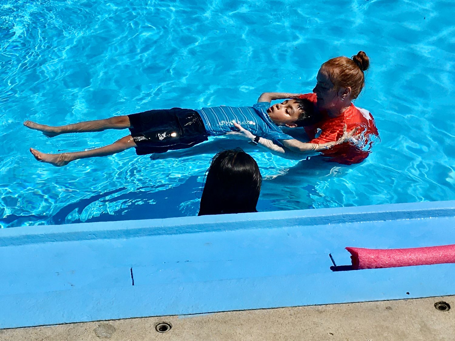 YMCA instructors support a student while they learn to float on their back during a swim lesson as part of the inaugural Learn to Swim program with GEHA in the summer 2022.