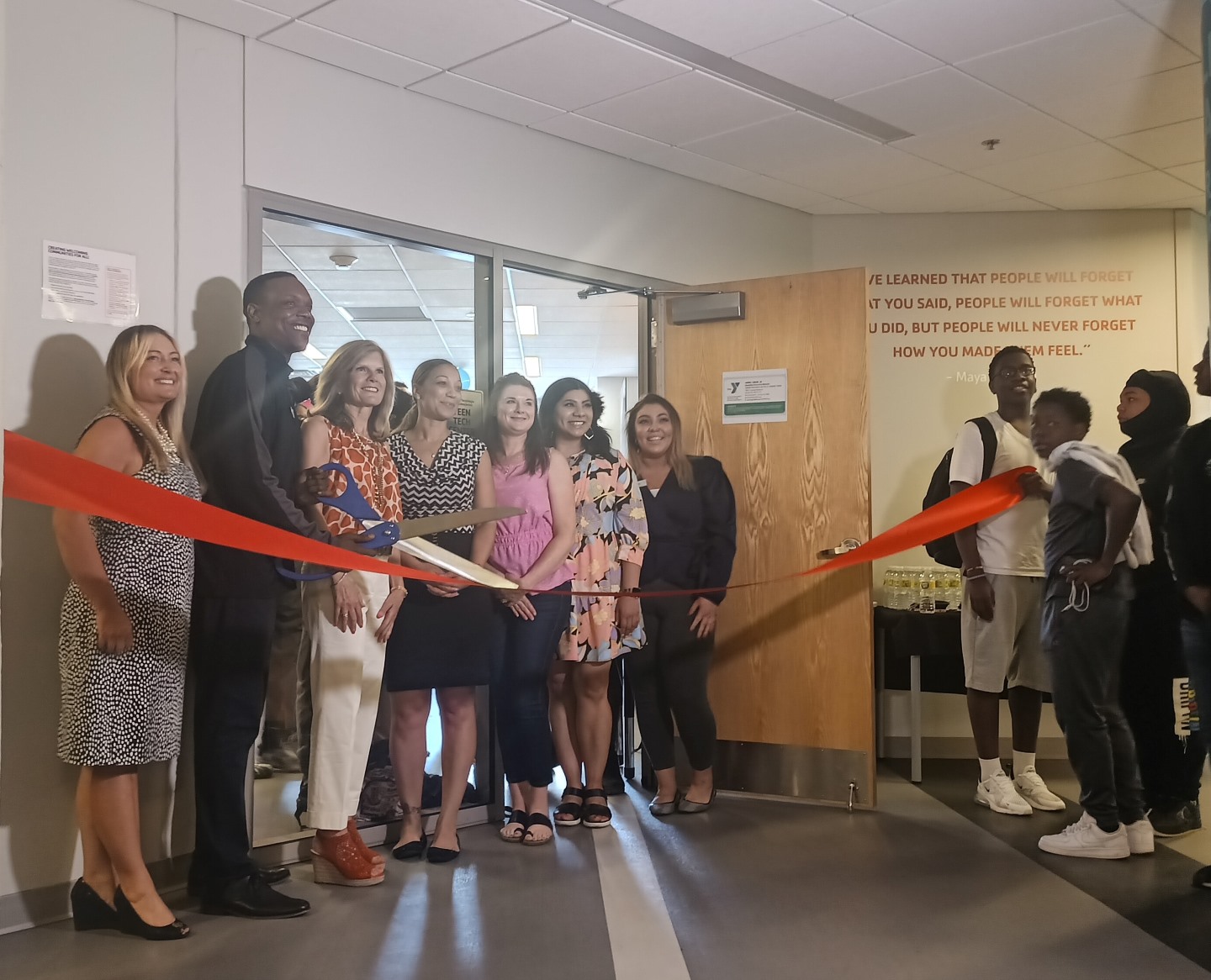 Staff and volunteers hold large ribbon and scissors in front of new teen tech center space at Linwood YMCA.