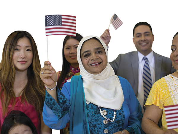 Group of people smiling while waving small American flags at naturalization ceremony.