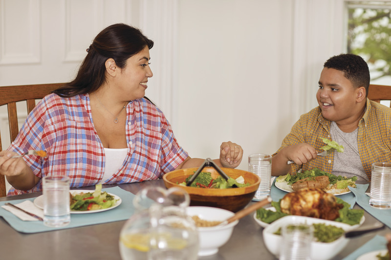 Mother and son sit at dinner table smiling as they eat a healthy meal.
