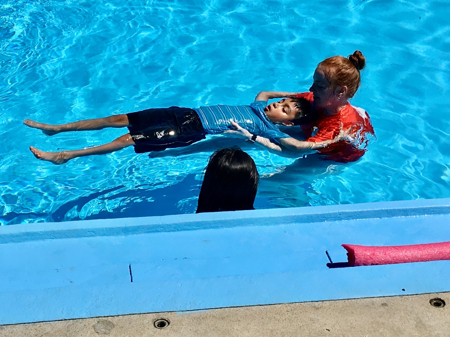 YMCA instructors helps a student float on their back during a swim lesson as part of the inaugural Learn to Swim program with GEHA in summer 2022.