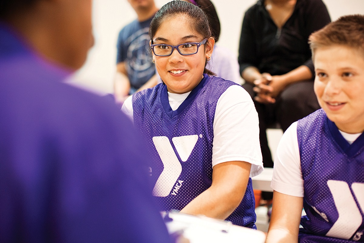 Two teen YMCA members talking with a YMCA coach.