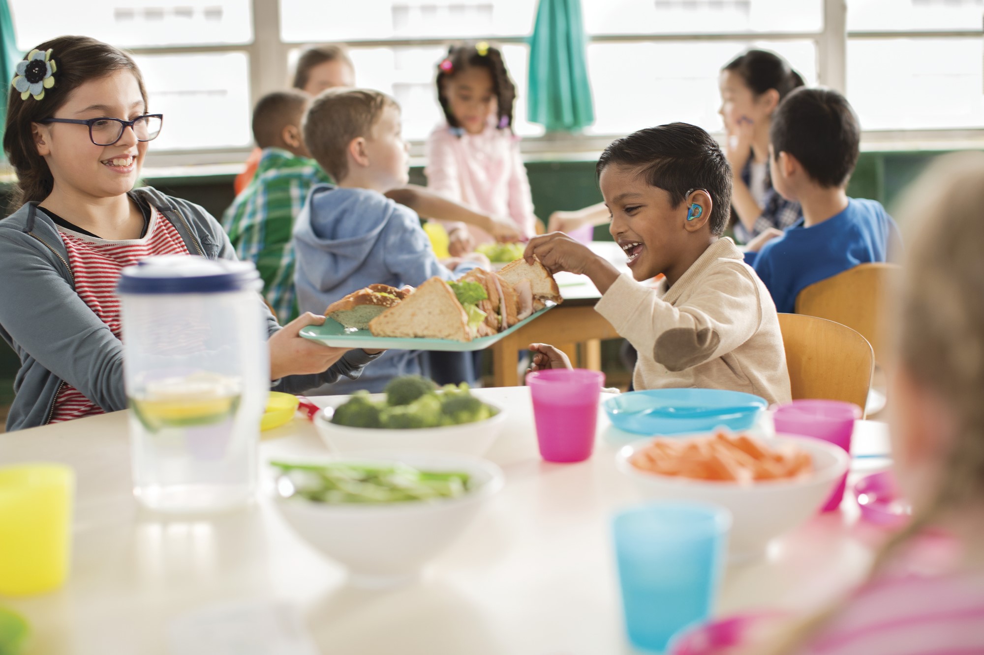 A group of children eat around a table. The table is filled with vegetables and other health foods.