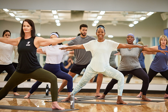 A group of YMCA members in the warrior 2 pose practicing yoga in a Kansas City YMCA group class.