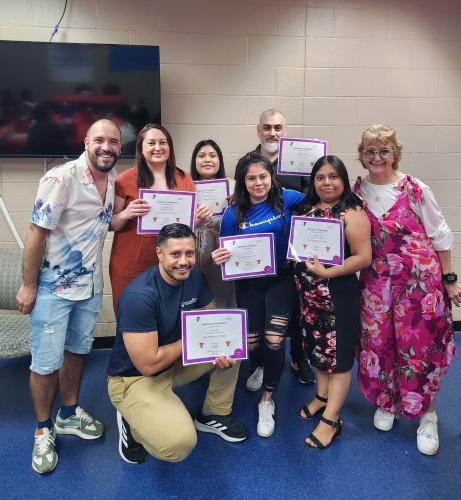 A group of eight ESL students pose for a photo with their completion certificates in a recent graduation ceremony