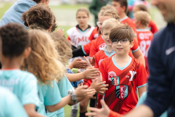 Young soccer players in red jerseys give high fives to teammates on a field