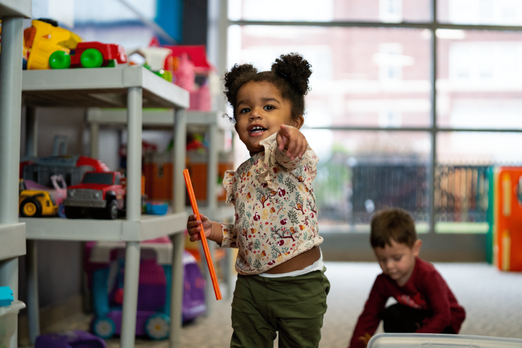 Toddler girl pointing and smiling in a colorful YMCA playroom with another child
