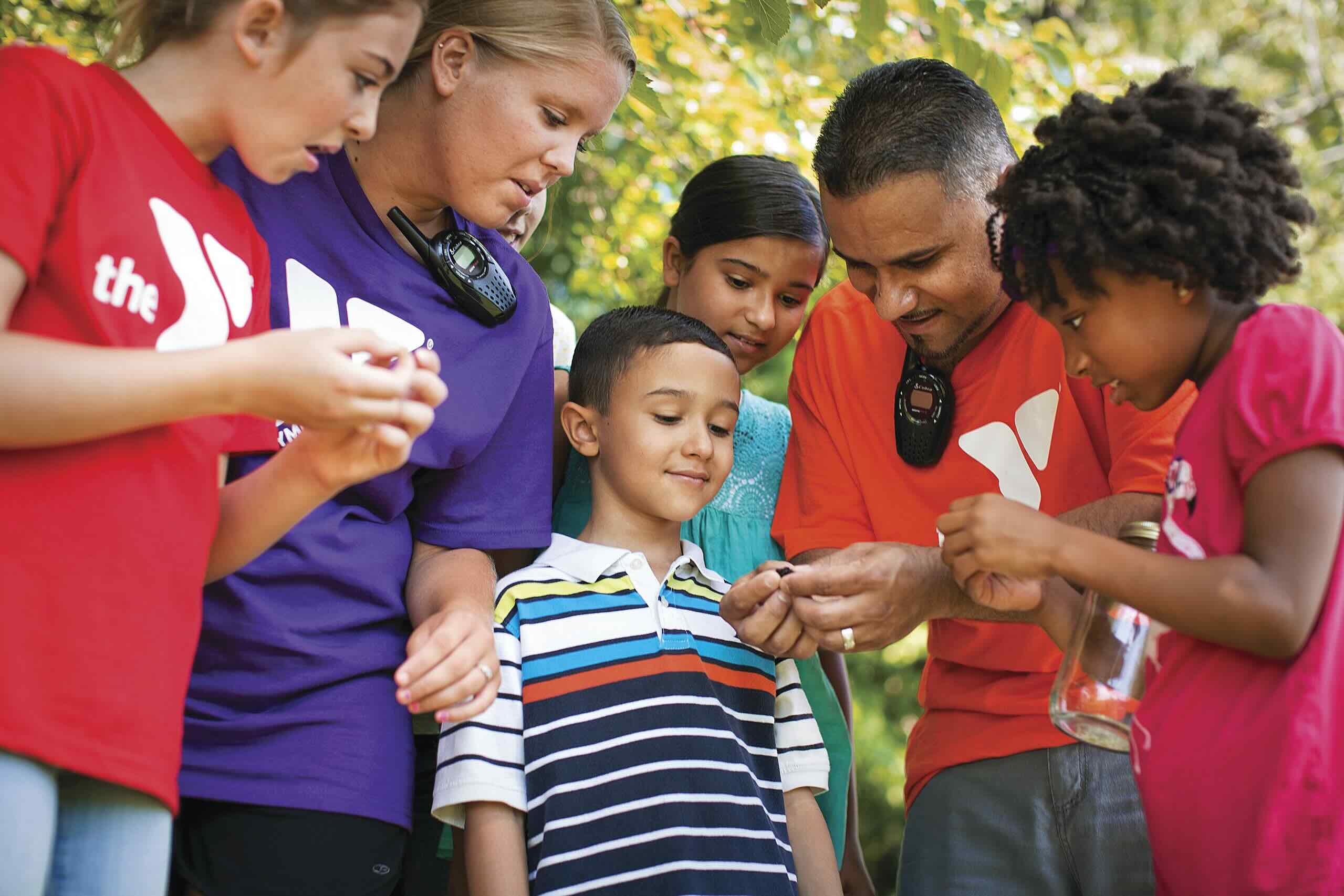 Two YMCA counselors and children examining nature discoveries together outdoors