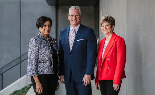 Three professionally dressed YMCA leaders standing together in business attire outdoors