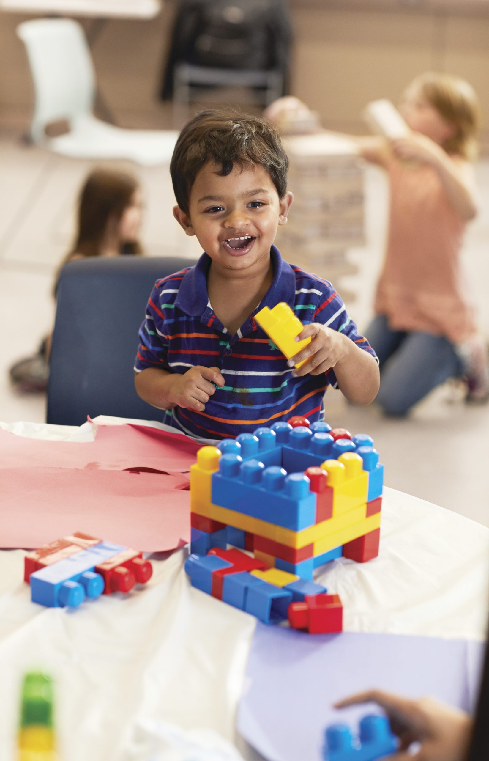 Smiling young boy building with colorful blocks at a table in a childcare room